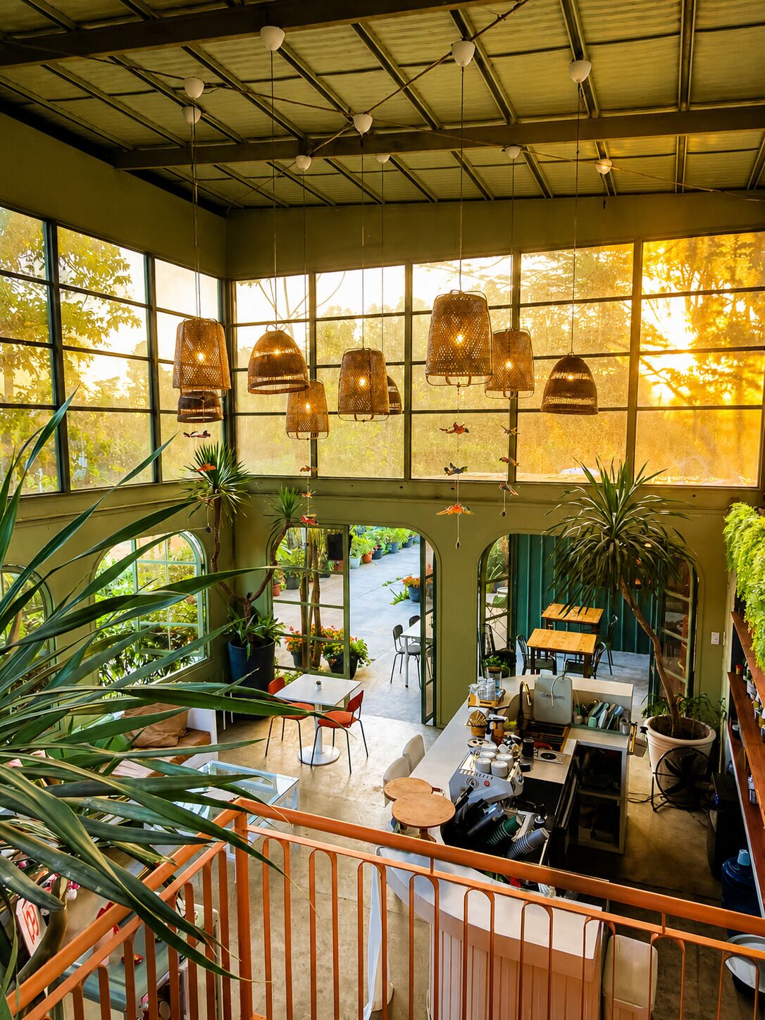 Una habitación amplia con grandes ventanales, lámparas colgantes y una variedad de plantas.