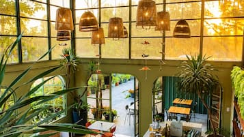 Una habitación amplia con grandes ventanales, lámparas colgantes y una variedad de plantas.