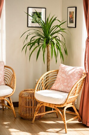 Une pièce avec des chaises en osier, un pouf rond et une grande plante en pot.