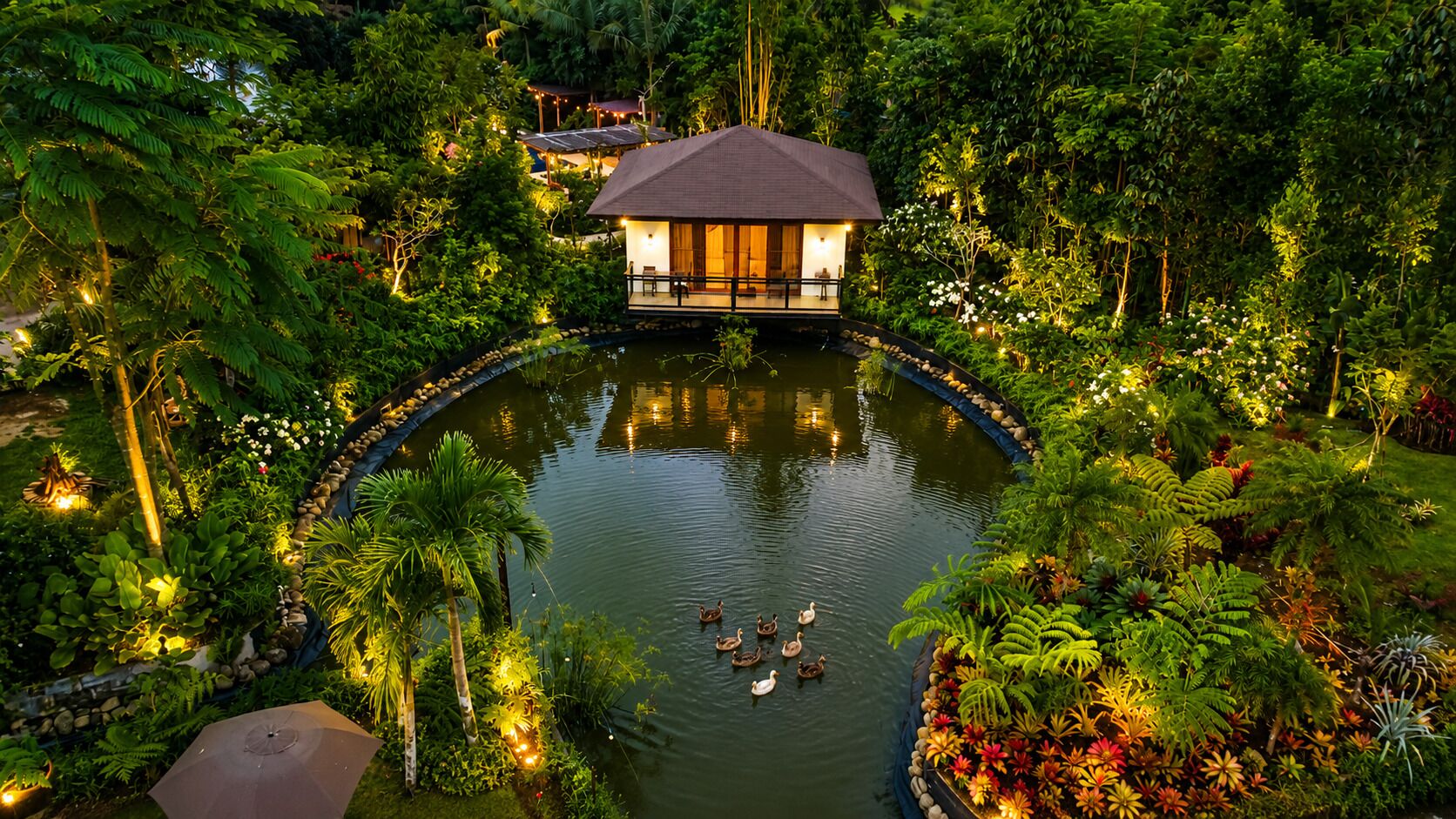 A pond with ducks, surrounded by lush greenery and a building with a thatched roof.