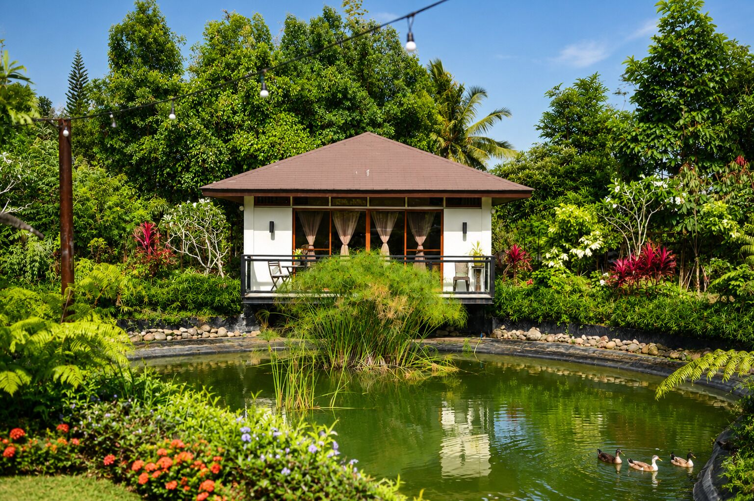 A traditional-style building with a tiled roof, surrounded by lush greenery and a small pond with ducks.