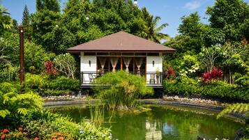 A traditional-style building with a tiled roof, surrounded by lush greenery and a small pond with ducks.