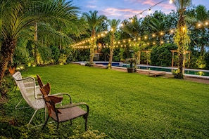 Un césped bien cuidado con piscina, luces colgantes y mobiliario exterior.