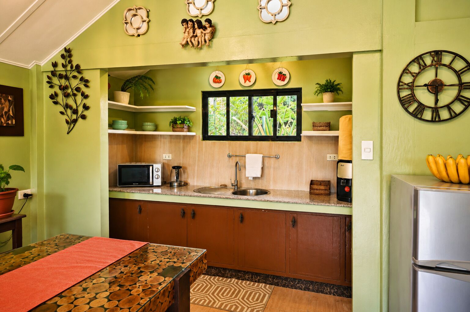 Una cocina con microondas, cafetera y un reloj en la pared.