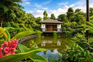 Un bâtiment de style traditionnel, avec un étang devant, entouré d’une végétation luxuriante.