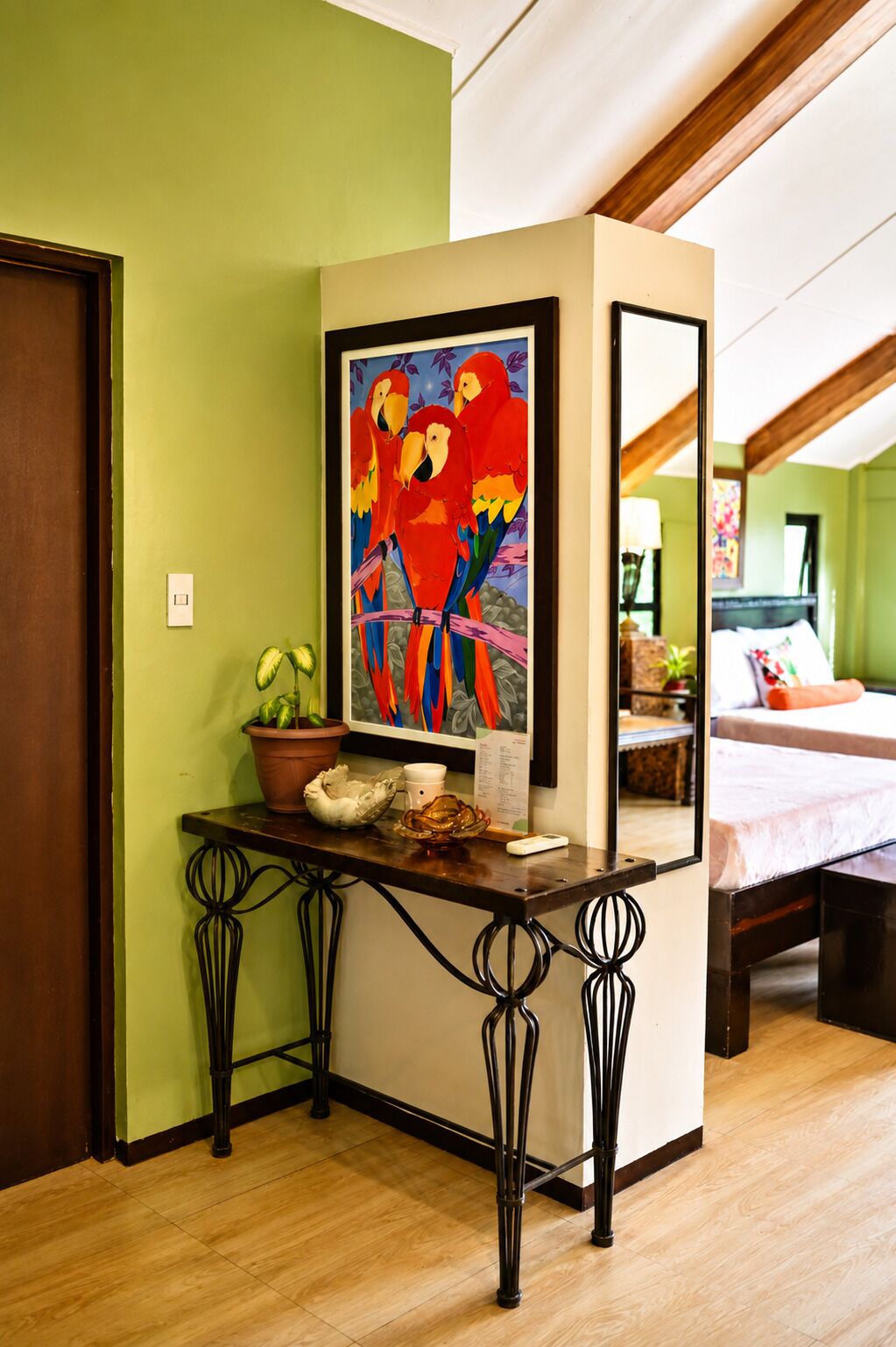 Une pièce comprenant un lit, un bureau avec un tableau, une plante en pot et un miroir qui reflète la pièce.