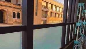 A balcony with a view of buildings, a window, and a metal rack. - Zen Apt in the Heart of Malta (Ta` Xbiex)