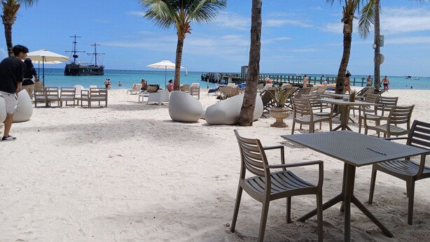 Een café aan het strand met terras, palmbomen en uitzicht op de oceaan.