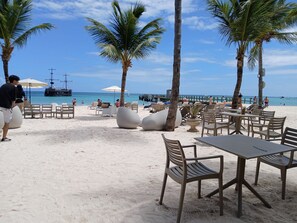 A beachside café with outdoor seating, palm trees, and a view of the ocean. - Villas Los Corales (Punta Cana)