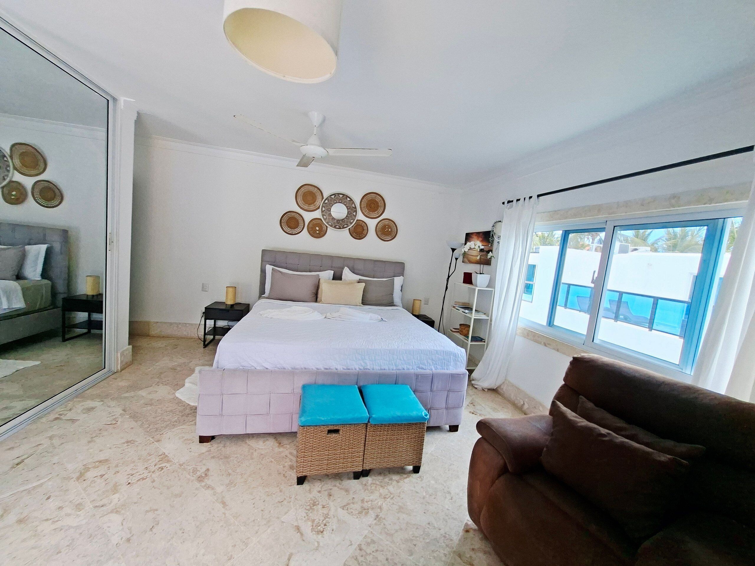 Un dormitorio con cama, ventilador de techo, ventana grande y vistas al exterior.