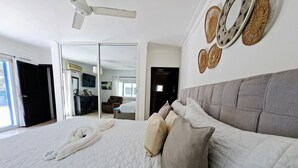 Een slaapkamer met een groot bed, een plafondventilator en een schuifdeur naar een badkamer.