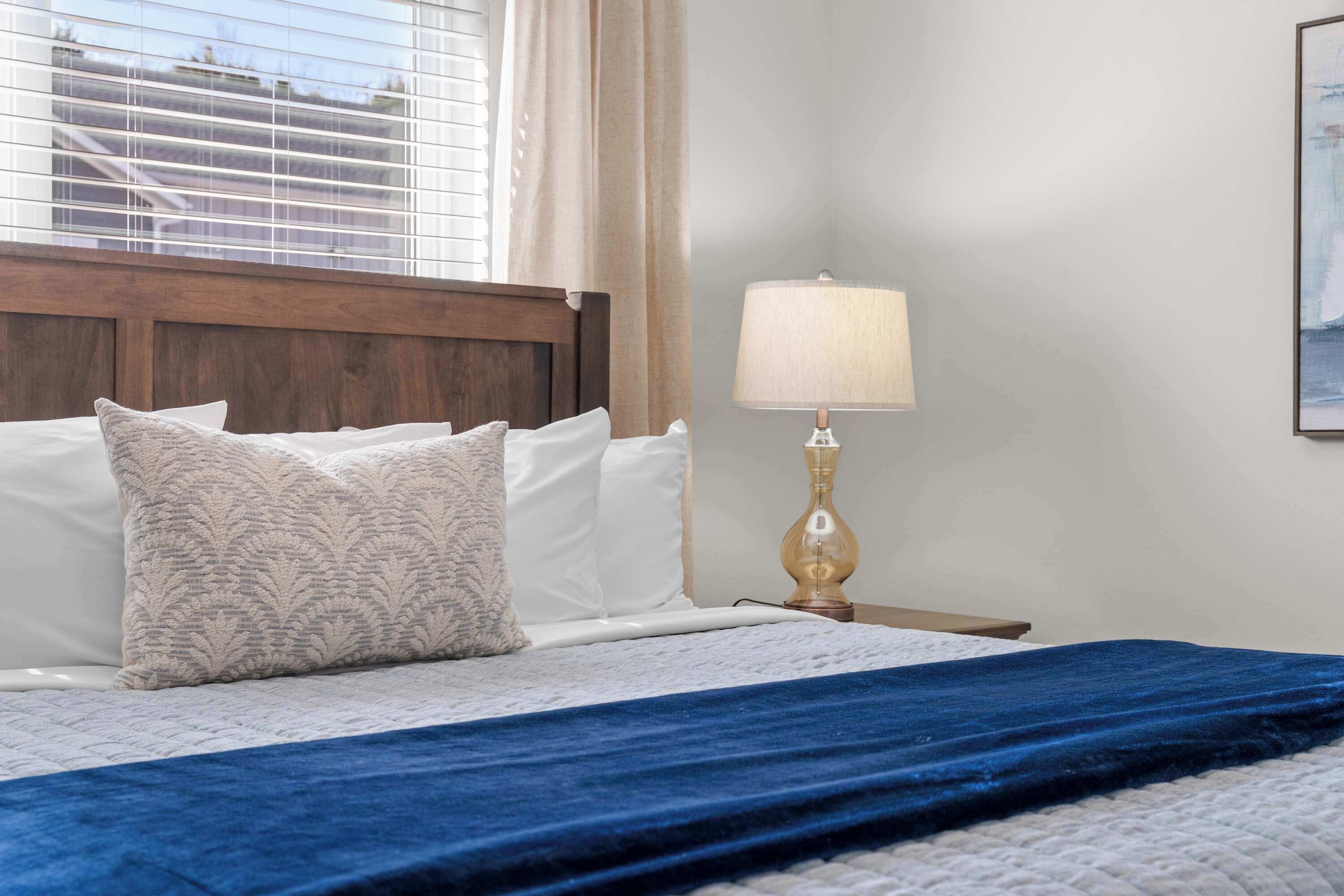 A neatly made bed with a blue blanket, a patterned pillow, and a bedside lamp on a wooden nightstand.