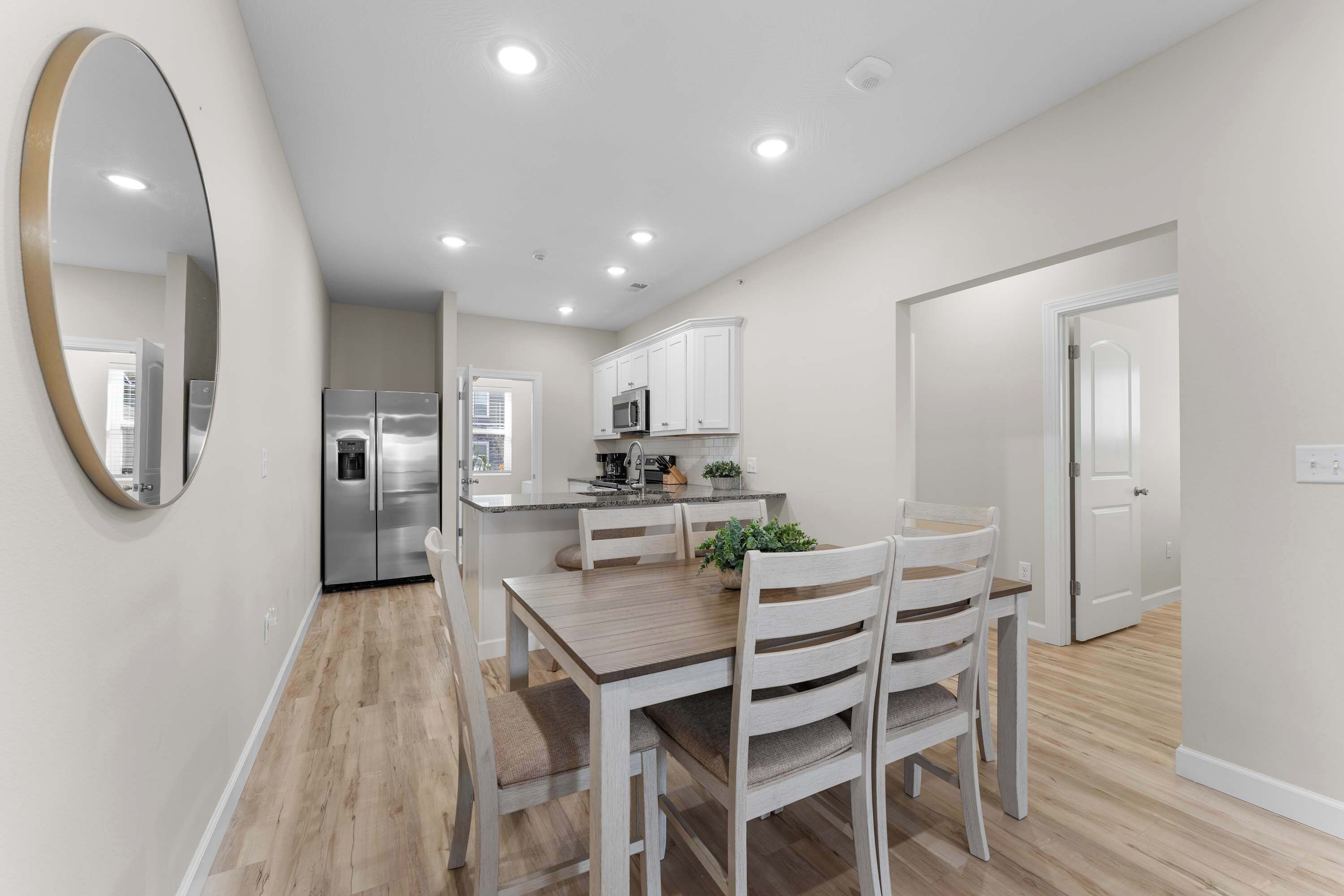 A modern kitchen with white cabinets, stainless steel appliances, and a dining area with a wooden table and chairs.
