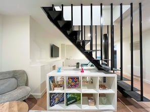 A modern living room with a staircase, a grey sofa, and a white shelving unit with board games. - 224 - Central Large Parisian Flat (París)