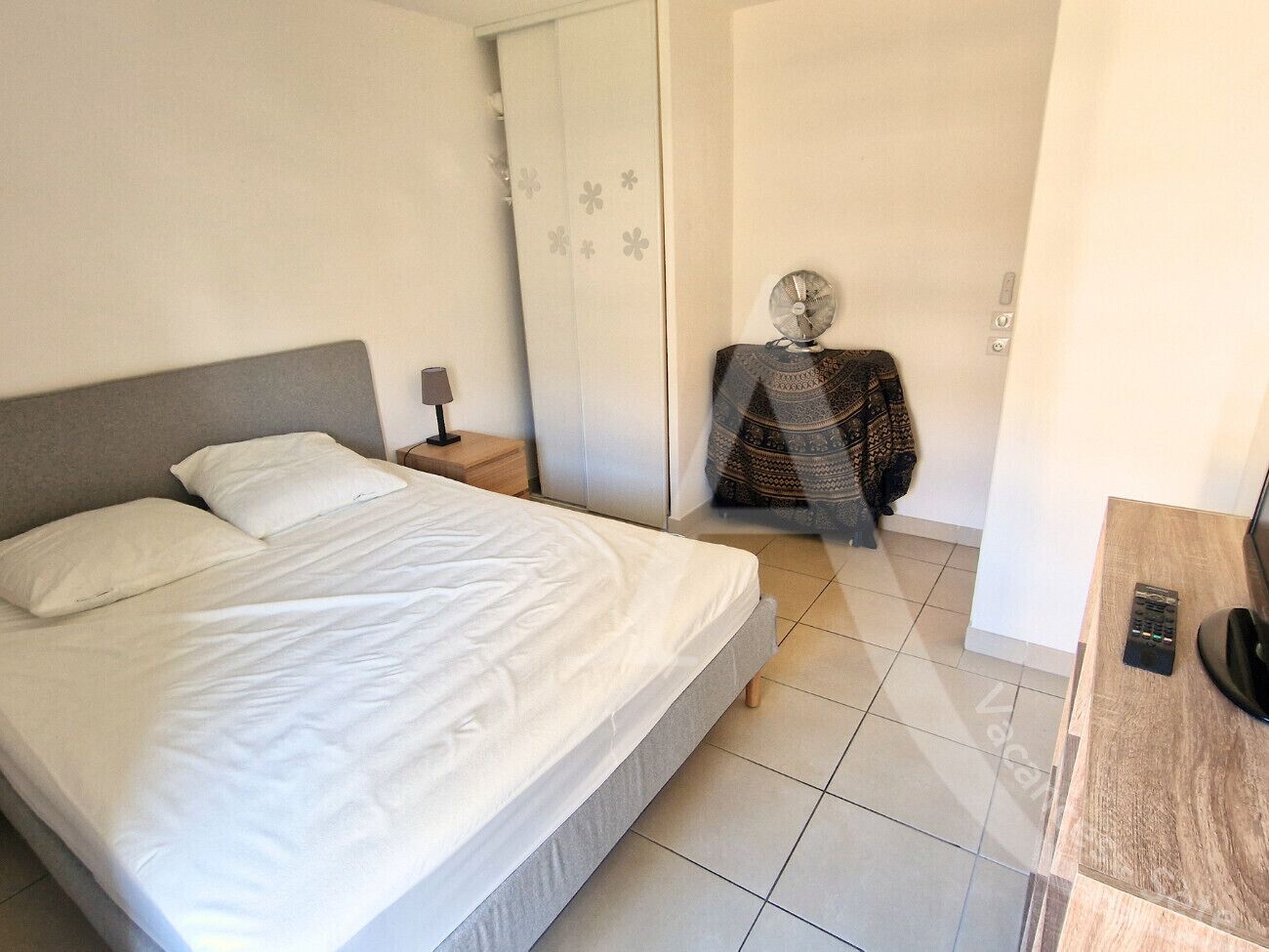 Une chambre à coucher comprenant un lit, une table de chevet, une lampe et une petite table ornée d’un objet décoratif.