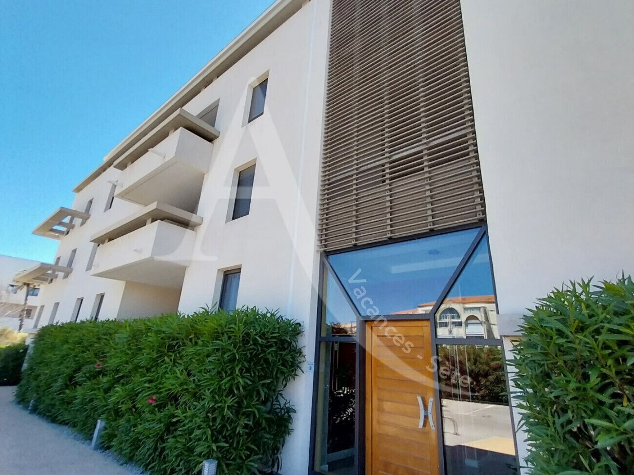 Un edificio moderno con facciata bianca, ampie finestre e una porta in legno.