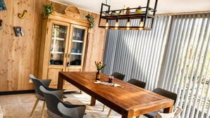 Ein Essbereich mit Holztisch, Stühlen, einem Schrank und einem Fenster mit vertikalen Jalousien.