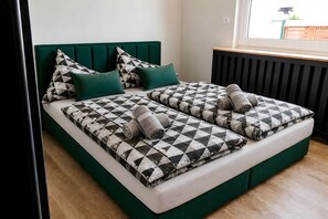 A double bed with a checkered bedspread, green headboard, and matching pillows. - Buddelhuus – Your Favorite Holiday Home by the North Sea (Norden)