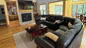 A living room with a fireplace, leather sofa, wooden bookshelf, and large windows.