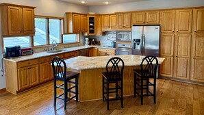 A modern kitchen with wooden cabinets, stainless steel appliances, a granite countertop, and a large island with bar stools.