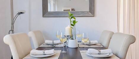 A dining table set for four with white plates, silverware, and glasses, flanked by two chairs, a candle centerpiece, and a mirror above.
