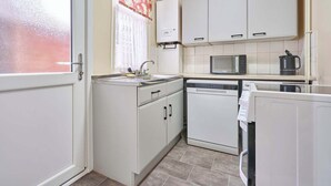 Cocina compacta con alacenas blancas, microondas, lavavajillas y ventana con cortina.