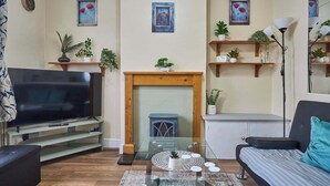 Una sala de estar con televisor, chimenea, sofá y plantas decorativas.