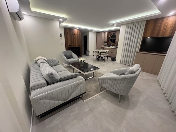 A modern living room with a sofa, armchairs, a coffee table, and a dining area with a table and chairs.
