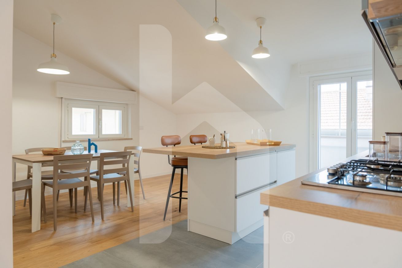 A modern kitchen with a central island, wooden chairs, pendant lighting, and a visible stove.