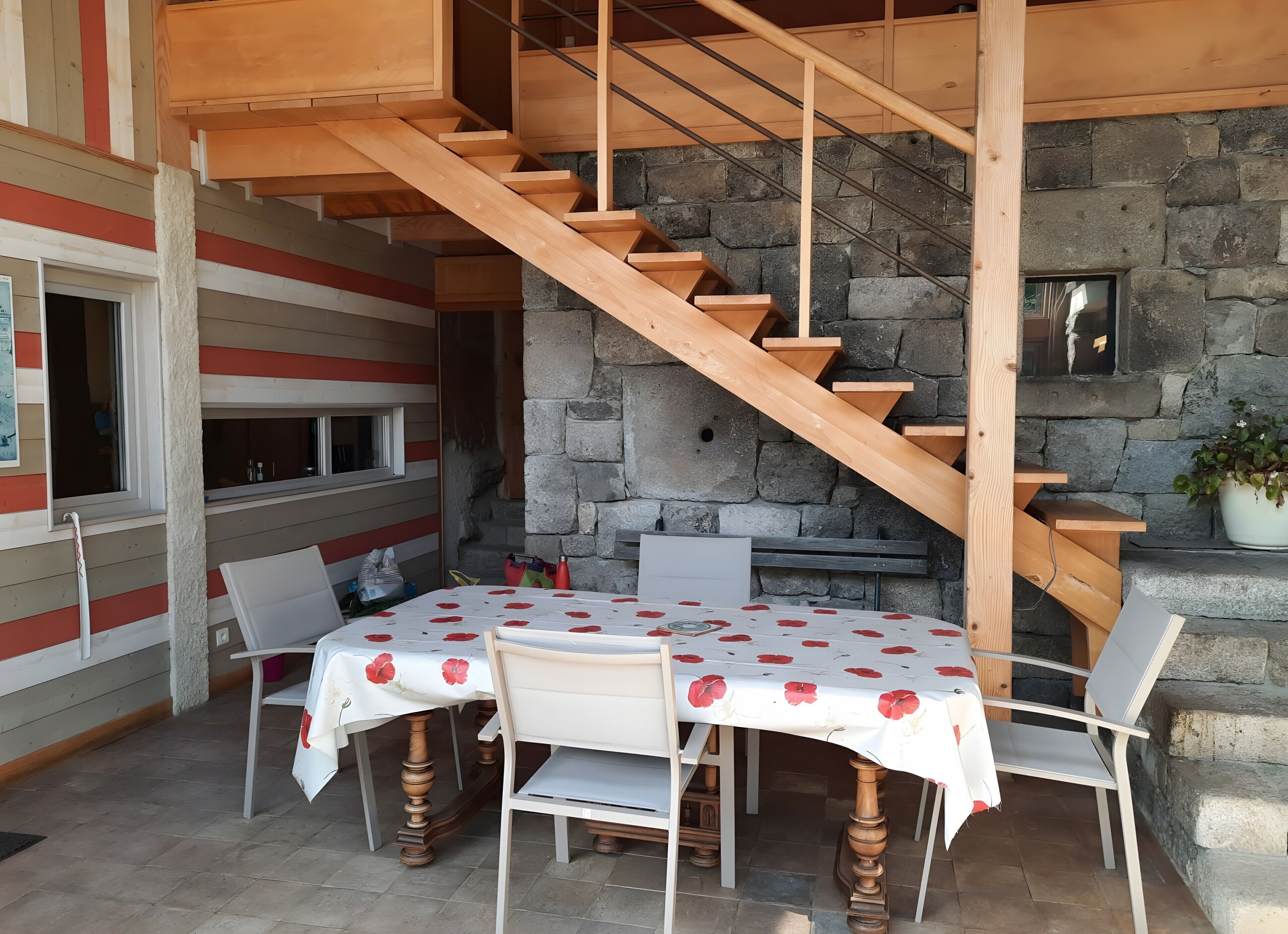 A wooden staircase leading to a stone wall, a round table with chairs, and a window with a view.
