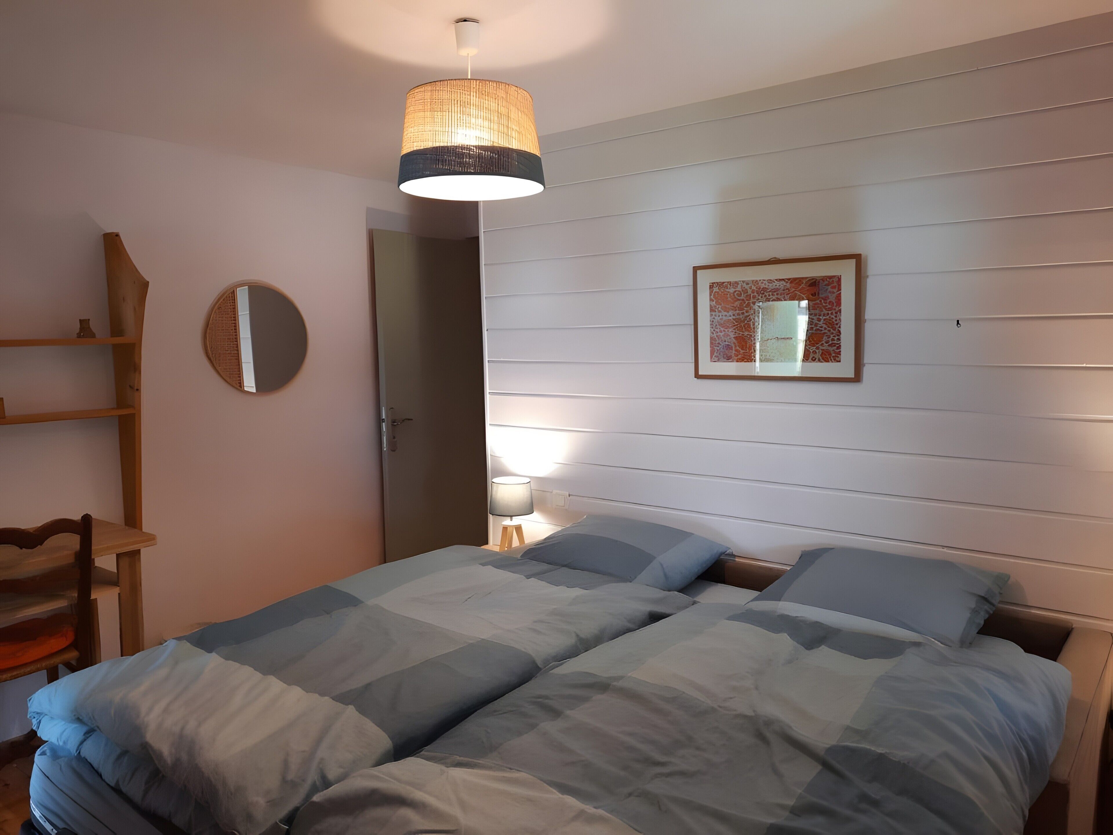 Une chambre à coucher avec un lit, une lampe de chevet, un miroir et une étagère en bois.