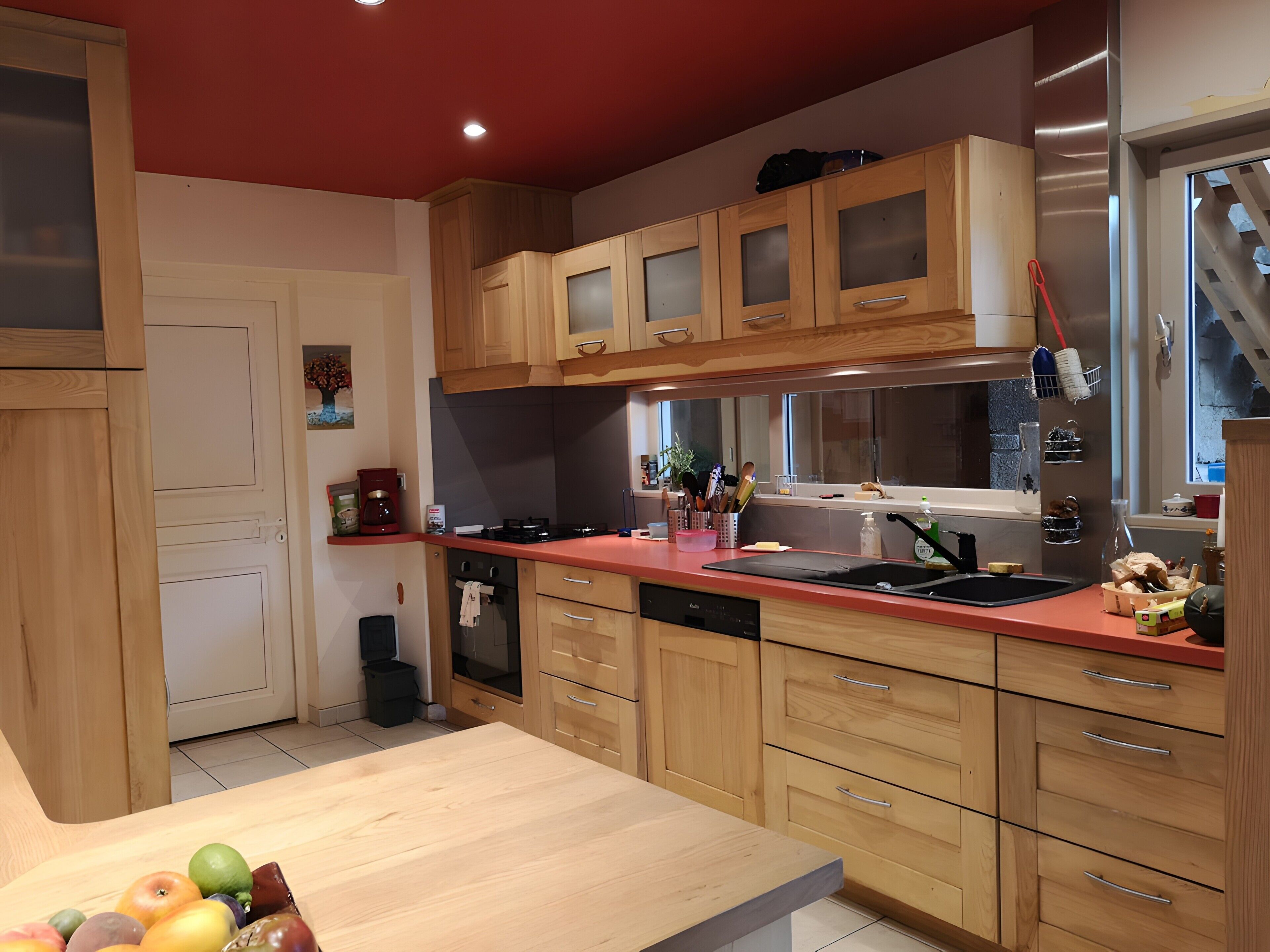 Una cocina con armarios de madera, encimera roja, lavavajillas y un lavabo.