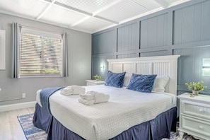 A bedroom with a large bed, a nightstand, a window with blinds, and a ceiling with a grid pattern.