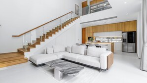 Una sala de estar moderna con un sofá seccional, una mesa de centro de mármol y una escalera que conduce a un nivel superior.