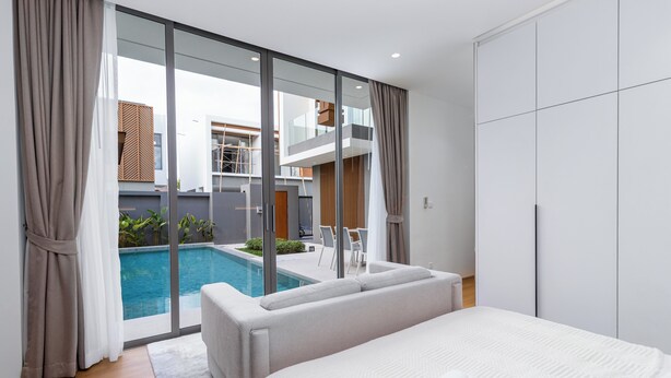 Una habitación de hotel moderna con una cama grande, un vidrio que da a una piscina y vistas del exterior del edificio.