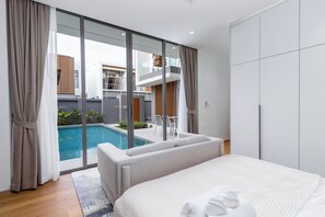 A modern hotel room with a large bed, a glass door leading to a pool, and a view of the building's exterior. - Brand New 3 bedroom Elite Pool Villa in Phuket (Tambon Choeng Thale)