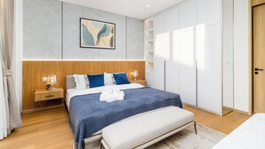 Una habitación de hotel moderna con una cama grande, mesitas de noche, un armario y un cuadro en la pared.