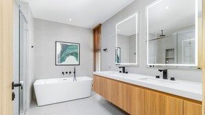 Un baño moderno con una bañera independiente, un espejo grande y un mueble de tocador de madera.