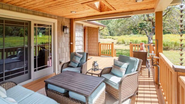 Een overdekt terras buiten met rieten meubilair, een tafel en uitzicht op de tuin.