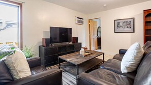 A living room with a TV, black furniture, a wooden coffee table, and a door leading to another room.