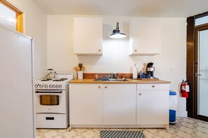 A compact kitchen with a stove, oven, and sink, white cabinets, and a fire extinguisher.