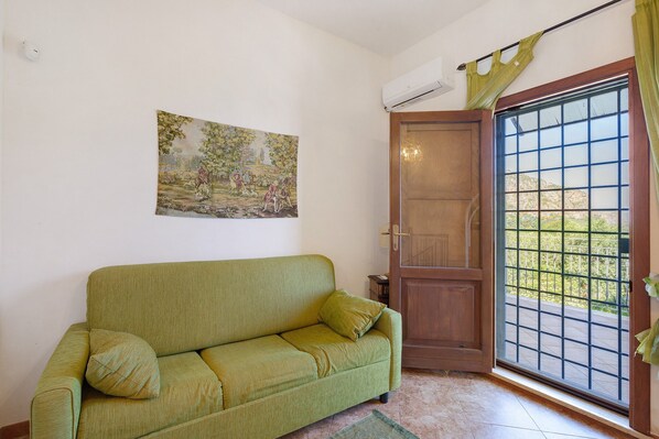 Una habitación con un sofá verde, una puerta con ventana y un cuadro en la pared.
