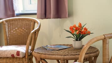 A wicker chair with a cushion, a small table with a potted plant and a magazine, and a window with curtains.