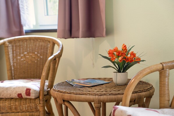 A wicker chair with a cushion, a small table with a potted plant and a magazine, and a window with curtains.