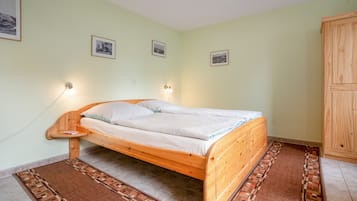 A single-bed room with a wooden frame, two bedside lamps, a patterned rug, and a wooden wardrobe.