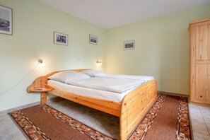 A single-bed room with a wooden frame, two bedside lamps, a patterned rug, and a wooden wardrobe.