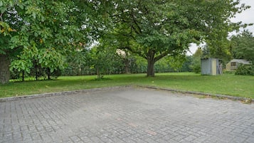 Un patio empedrado con un árbol grande y un cobertizo pequeño.