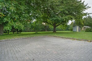 Une cour dallée avec un grand arbre et un petit abri de jardin.