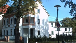Un immeuble à plusieurs étages, doté d’une façade blanche et de détails en briques rouges, d’un balcon bien visible et d’un lampadaire.