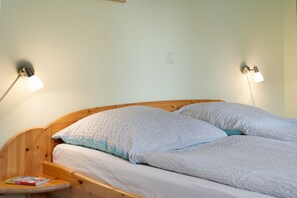 Un lit avec deux oreillers, une table de chevet avec un livre et deux lampes fixées au mur.